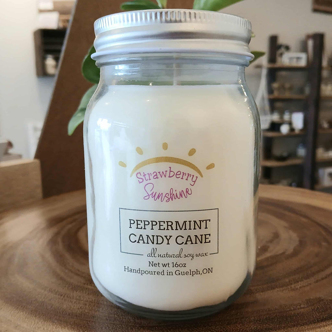 Jar of peppermint candy cane candle with 'Strawberry Sunshine' label on a wooden surface.