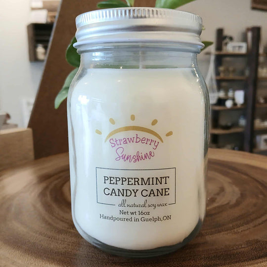 Jar of peppermint candy cane candle with 'Strawberry Sunshine' label on a wooden surface.