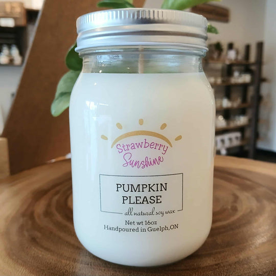 Candle in a jar labeled 'Pumpkin Please' with 'Strawberry Sunshine' branding on a wooden surface.