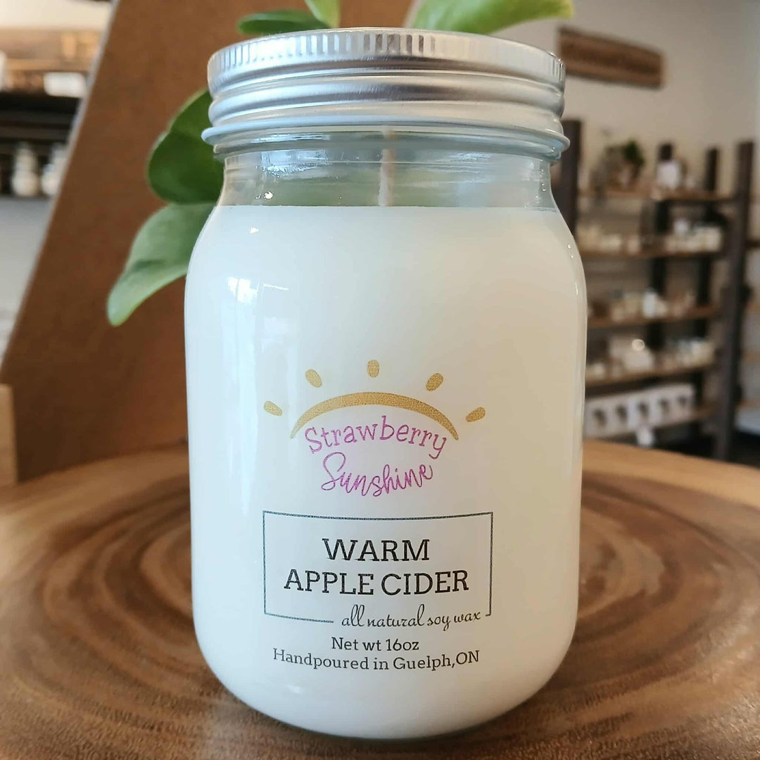 Jar of 'Warm Apple Cider' candle with 'Strawberry Sunshine' branding on a wooden surface.