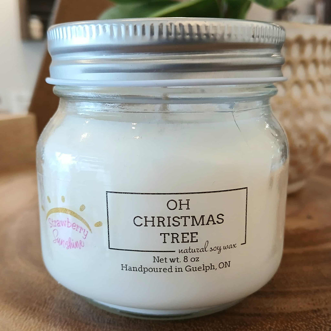 Jar of candle labeled 'Oh Christmas Tree' on a wooden surface