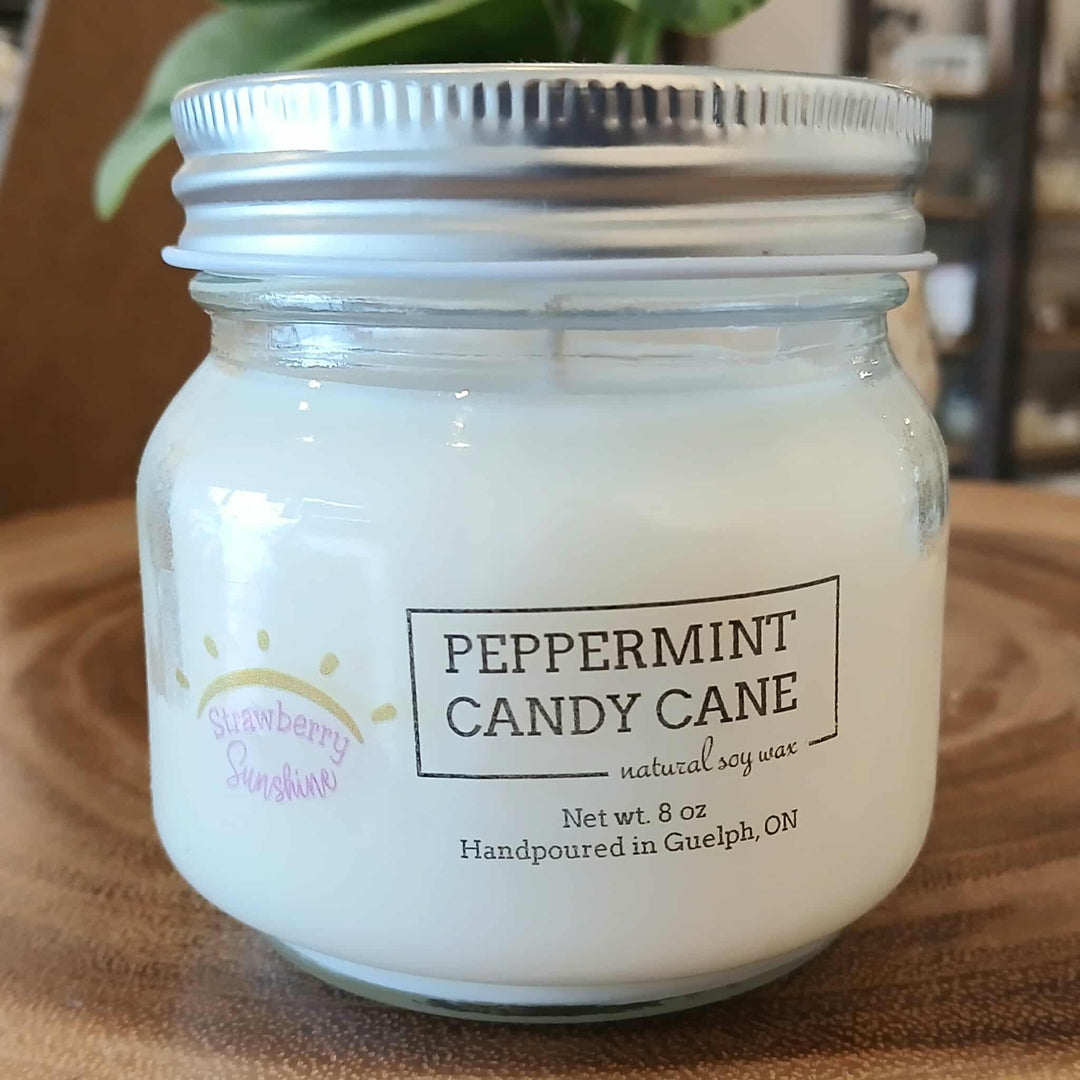 Candle in a glass jar labeled 'Peppermint Candy Cane' on a wooden surface.