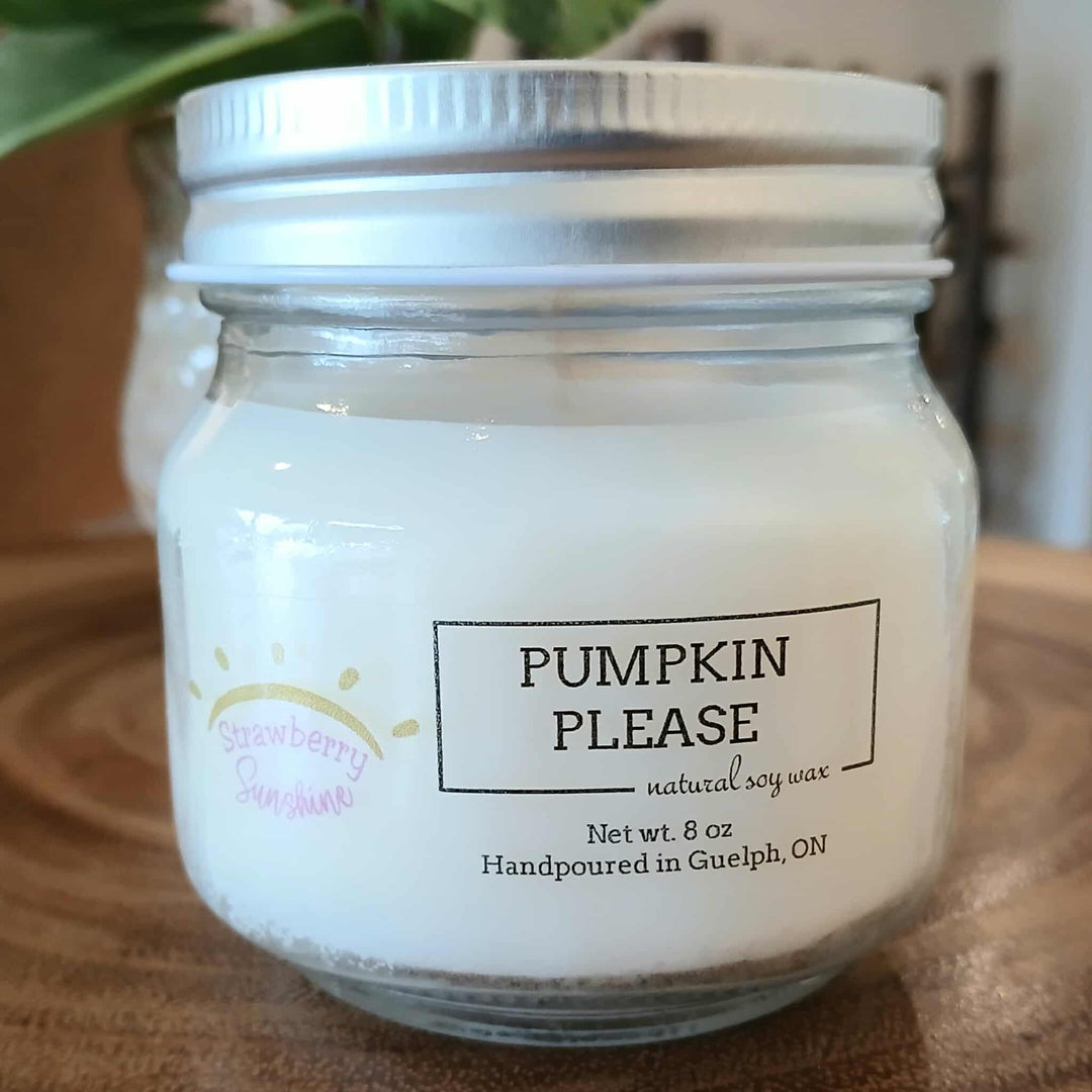 Jar of candle labeled 'Pumpkin Please' on a wooden surface