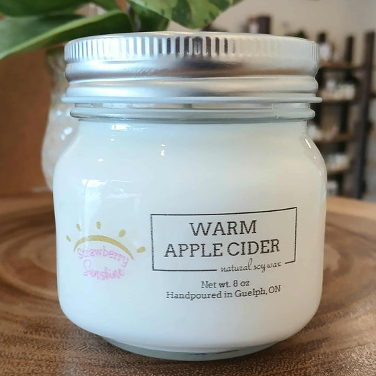 Candle jar labeled 'Warm Apple Cider' on a wooden surface with a blurred background