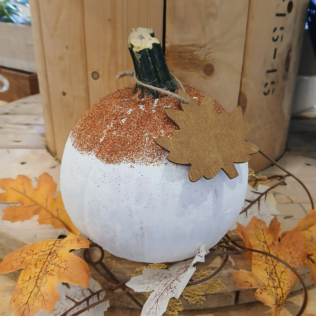 A white decorative pumpkin with a rustic autumn theme, featuring a textured copper-brown glittery top, a faux zucchini stem, a brown leaf accent, and surrounded by fake orange and yellow leaves.